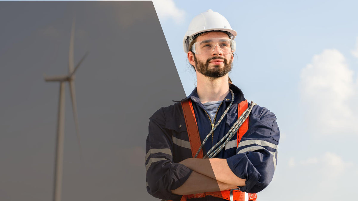 Engineer in hard hat, safety glasses and harness standing in front of a wind turbine, Delta Al Raqiya electrical supplier